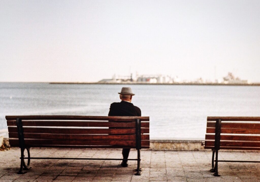 elderly man sitting on a bench overlooking a city harbor