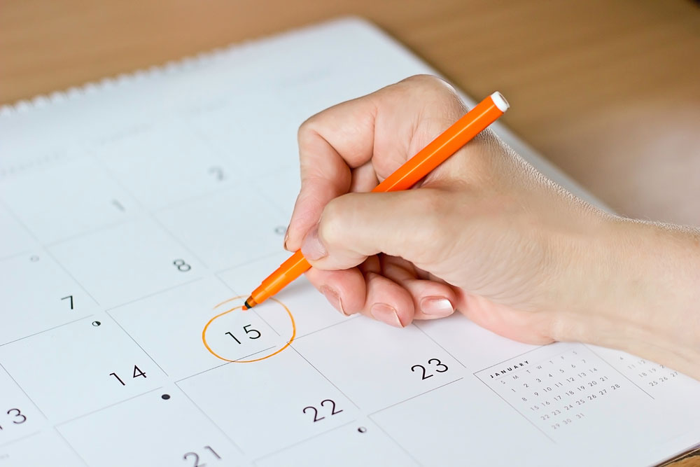 Hand with orange pen circling 15th day on a calendar