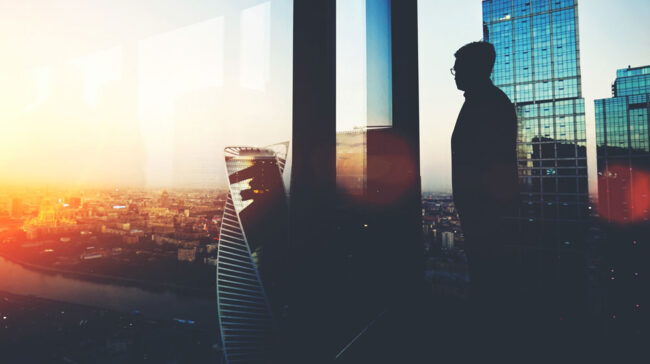 Independence-EFC Bespectacled business man looking out over city at dusk.