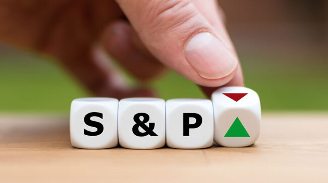 s-and-p-500 Finger turning wooden die that spell S-&-P with green up arrow or red down arrow.