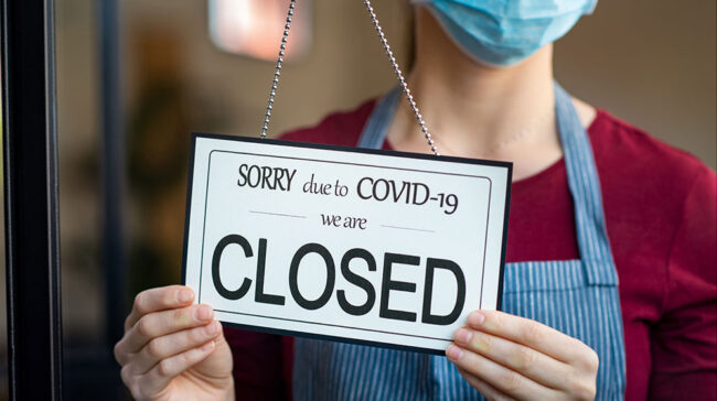 Retailer turning a door sign to: "SORRY due to COVID-19 we are CLOSED"