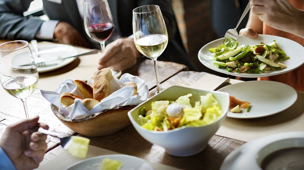 Business people at a lunch meeting sharing salad and drinking wine.