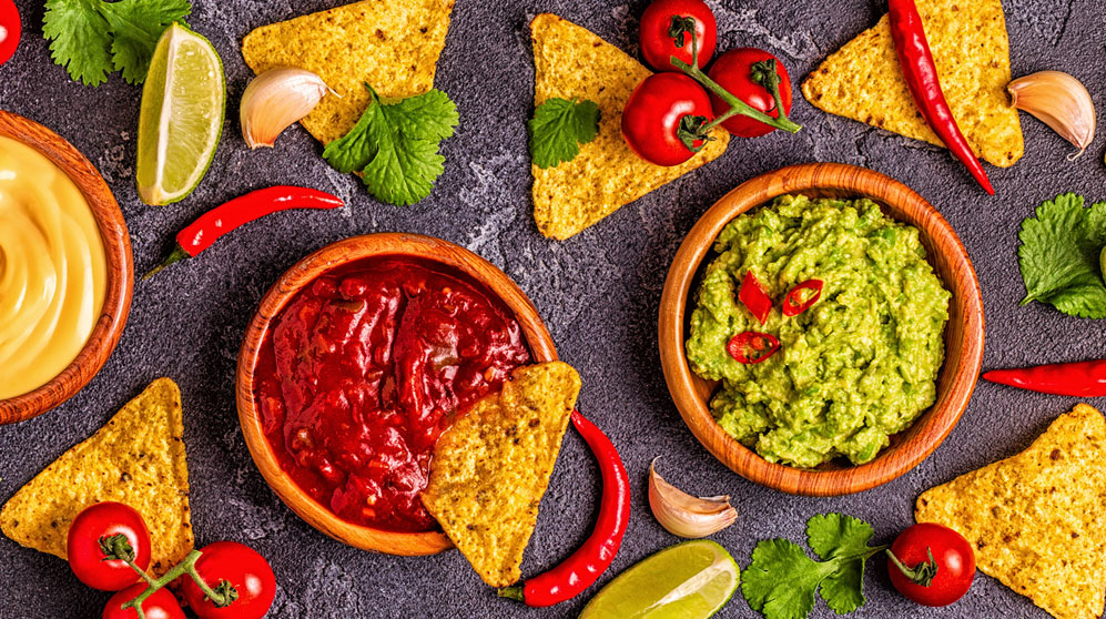 Bowls of guacamole, salsa, queso, chips, limes, peppers, cilantro.