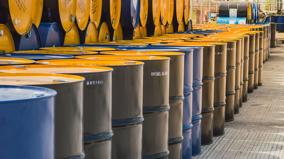 Hundreds of stacked black and blue oil barrels with yellow lids.