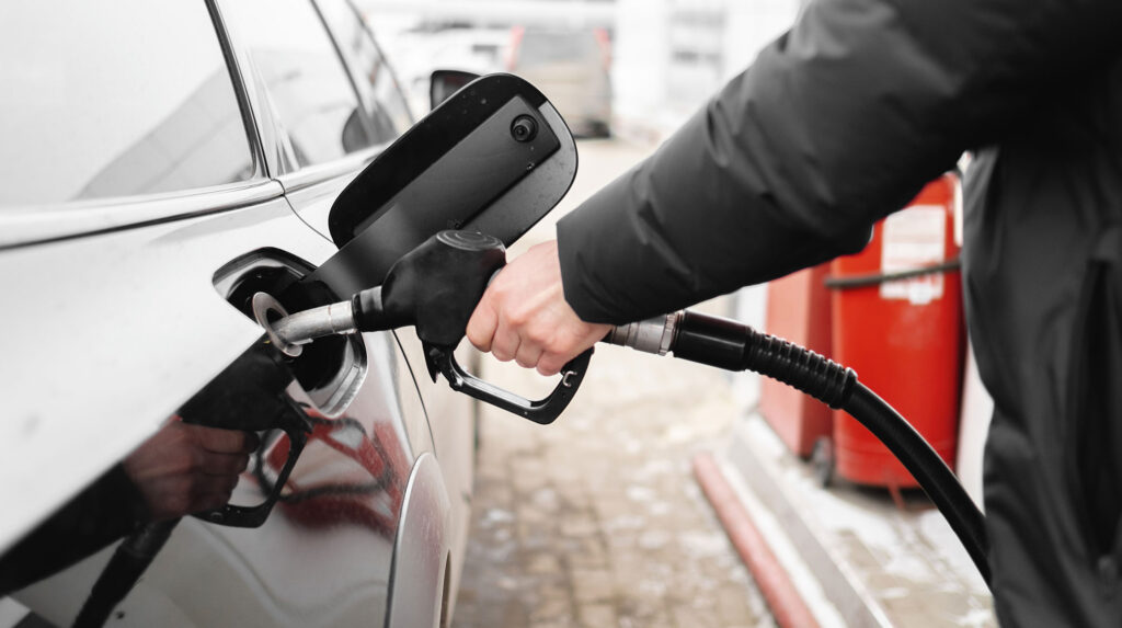 Arm holding a gas nozzle to car and filling tank.
