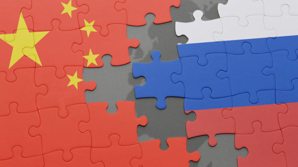 Jigsaw puzzle with pieces depicting China flag and Russia flag, separated by a border of empty pieces revealed shadow of EU.