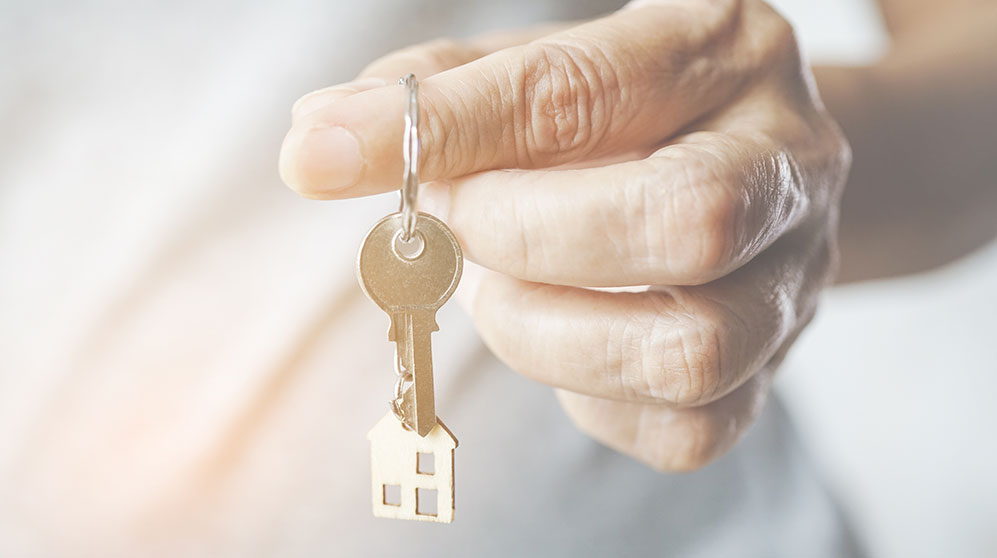 older person's hand holding key chain with house charm