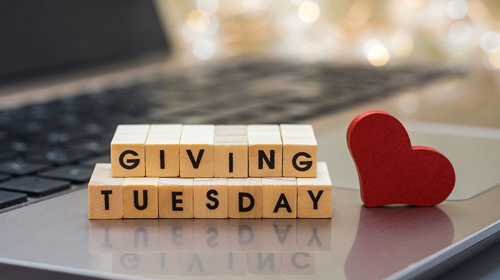giving tuesday spelled out in block letters on a laptop keyboard with wooden heart