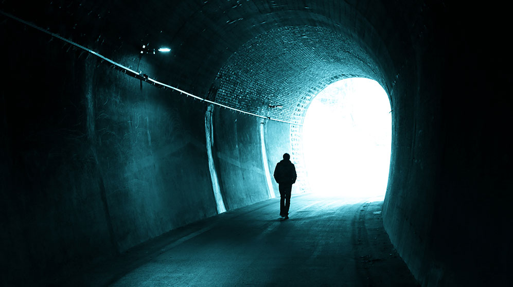person walking through a dark tunnel toward the light at the opening