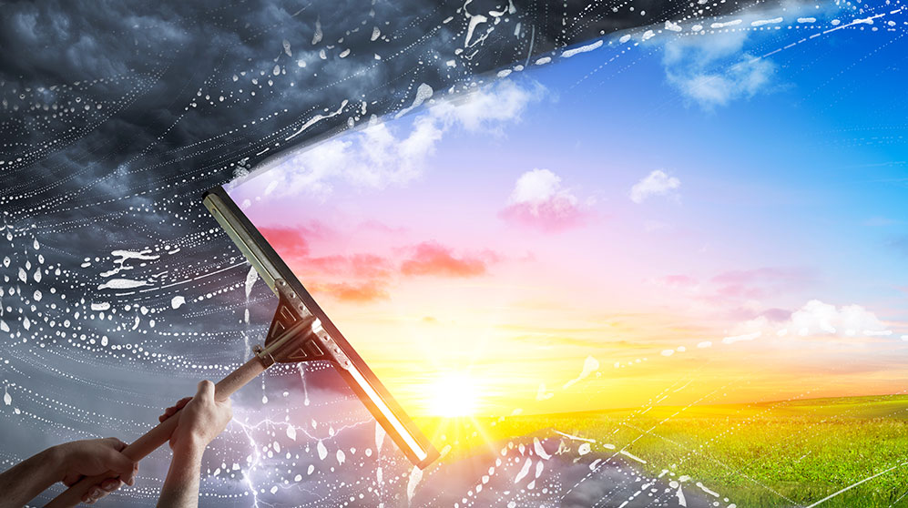 Image showing a person taking a squeegee to a stormy sky to reveal sunshine.