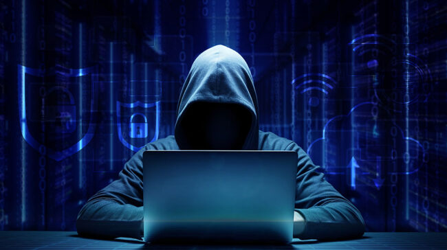 Photo of a hooded hacker on a computer