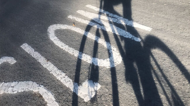Photo of pavement with "SLOW" written on it, along with the shadow of a biker